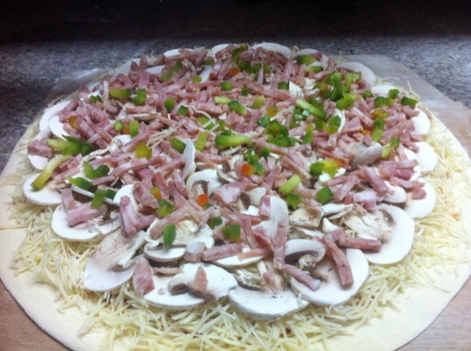 Une pizza crue garnie de jambon, champignons et poivrons avant enfournement